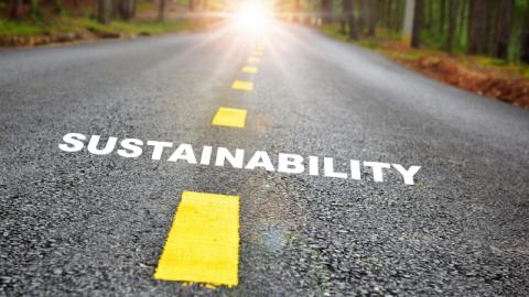 The word sustainability superimposed on road leading to sunset.